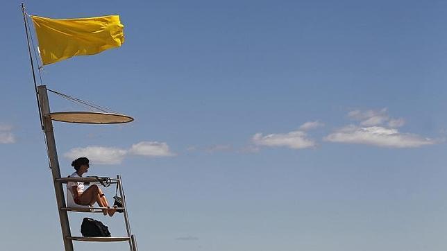 Una socorrista vigila a los bañistas en una playa con bandera amarilla, que aconseja precaución