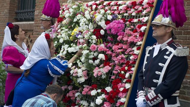 Vecinas y vecinos decoran con claveles un panel junt a la iglesia de La Paloma