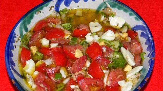 Una ensalada cuyos ingredientes básicos son la cebolla, tomate, pimiento verde, pescado y pepino