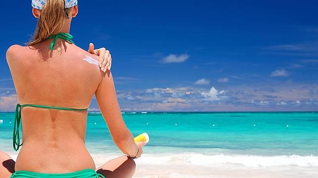 Una mujer se aplica crema solar en una playa