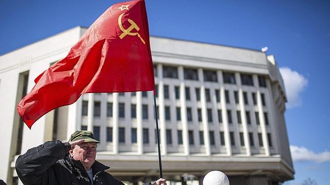 Un hombre sostiene una bandera soviética mientras realiza un saludo militar delante del Parlamento, tras el referéndum en el que el 96,77 % de los votantes crimeos mostró su apoyo ayer a favor de la reunificación con Rusia, en Simferópol, en la península ucraniana de Crimea hoy, lunes 17 d
