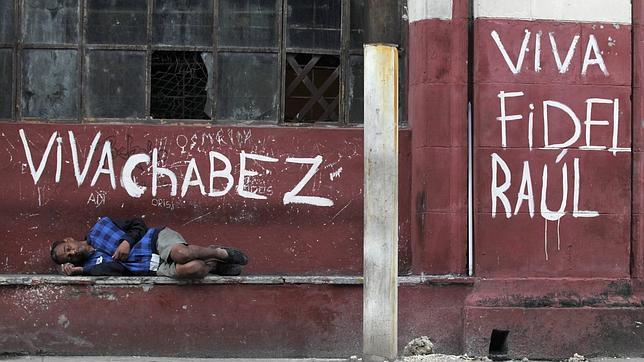 Un cubano descansa junto a un grafiti partidario del castrismo y del chavismo en una calle de La Habana