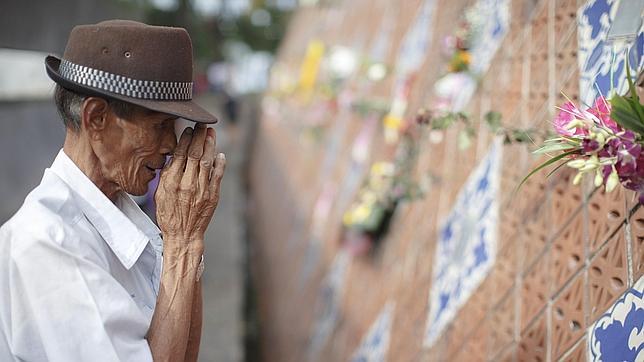 Un hombre reza frente a la placa con el nombre de sus familiares en un monumento en el pueblo pesquero de Ban Nam Khem