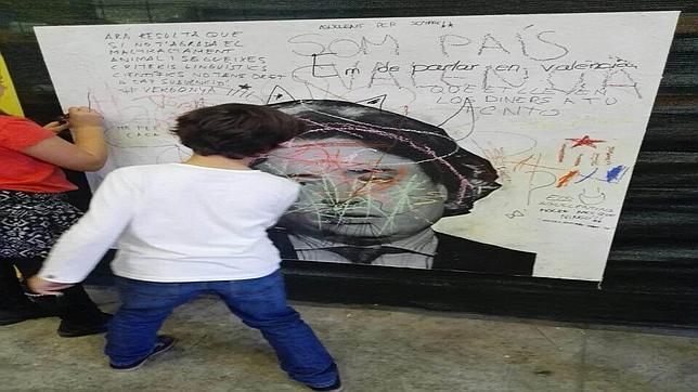 Un niño pinta sobre una fotografía del conseller Santamaría en el acto organizado por Escola Valenciana