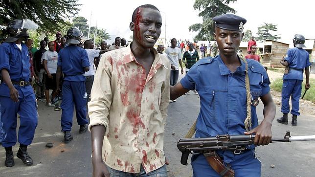un policía antidisturbios escolta a un herido en las protestas, en Bujumbura