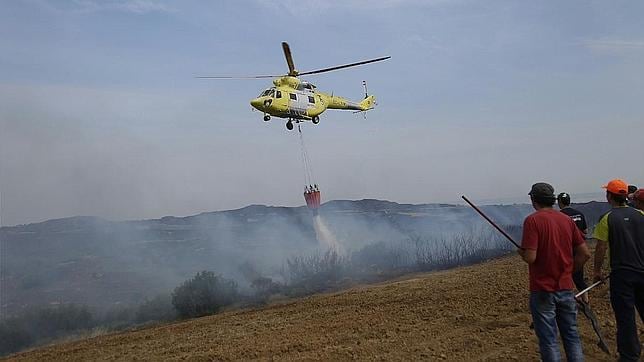Un helicóptero descarga agua sobre uno de los focos del incendio ante la mirada de varios voluntarios