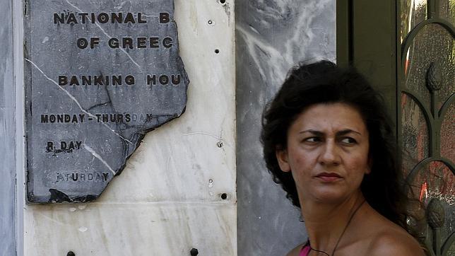 Una mujer pasa junto a un letrero roto de una sede bancaria griega en Atenas