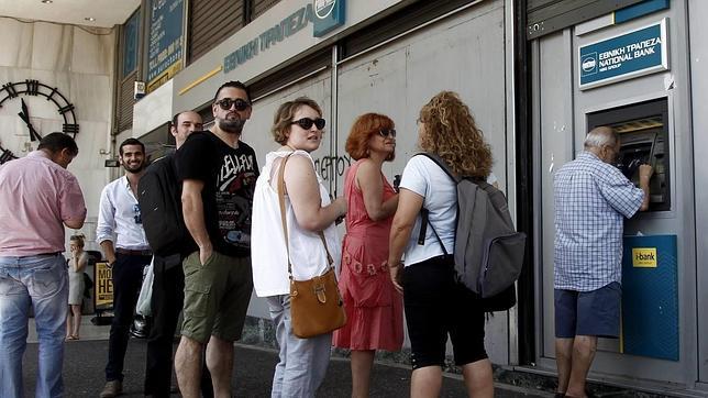 Atenienses hacen cola para retirar dinero de un cajero automático en una sucursal del Banco Nacional de Grecia, en Atenas