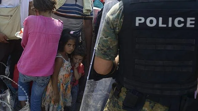 Un grupo de inmigrantes controlados por la Policía macedonia cruzan la frontera entre Macedonia y Grecia