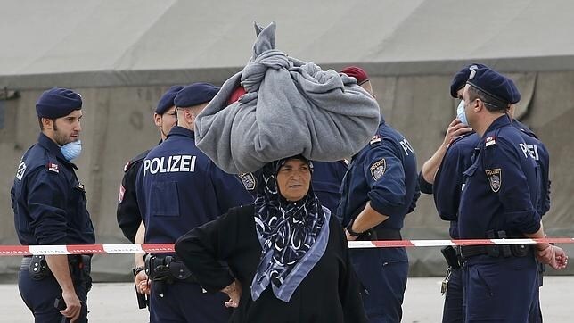Una mujer extranjera, con sus pertencencias sobre la cabeza, junto a agentes húngaros en Nickelsdorf, Austria