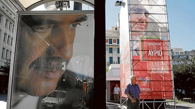 Un hombre camina entre las pancartas de los líderes de Syriza (derecha) y Nueva Democracia