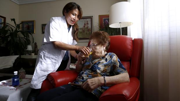 Una trabajadora de la ayuda a domicilio da de beber a una usuaria del servicio