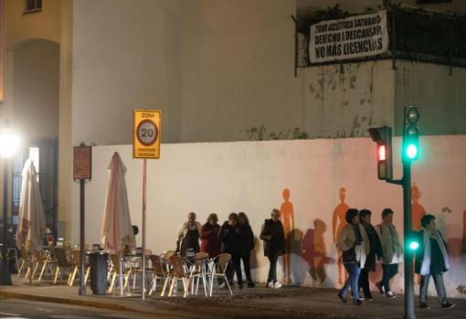 Varias personas pasan debajo de un cartel de protesta de los vecinos por los ruidos