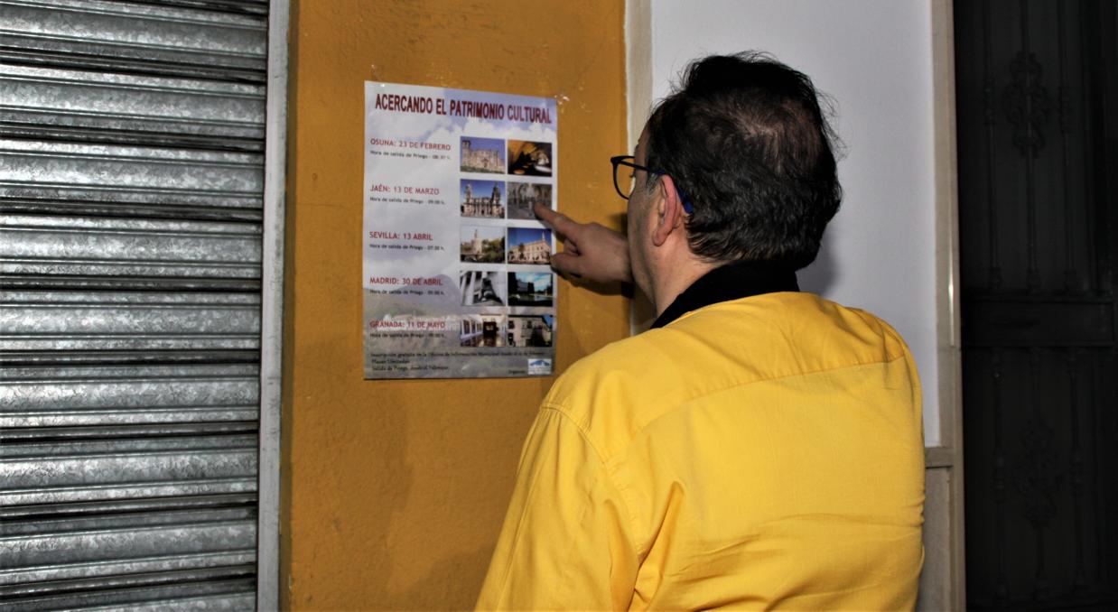 Un vecino ante un cartel que anuncia los viajes gratis del Ayuntamiento de Priego