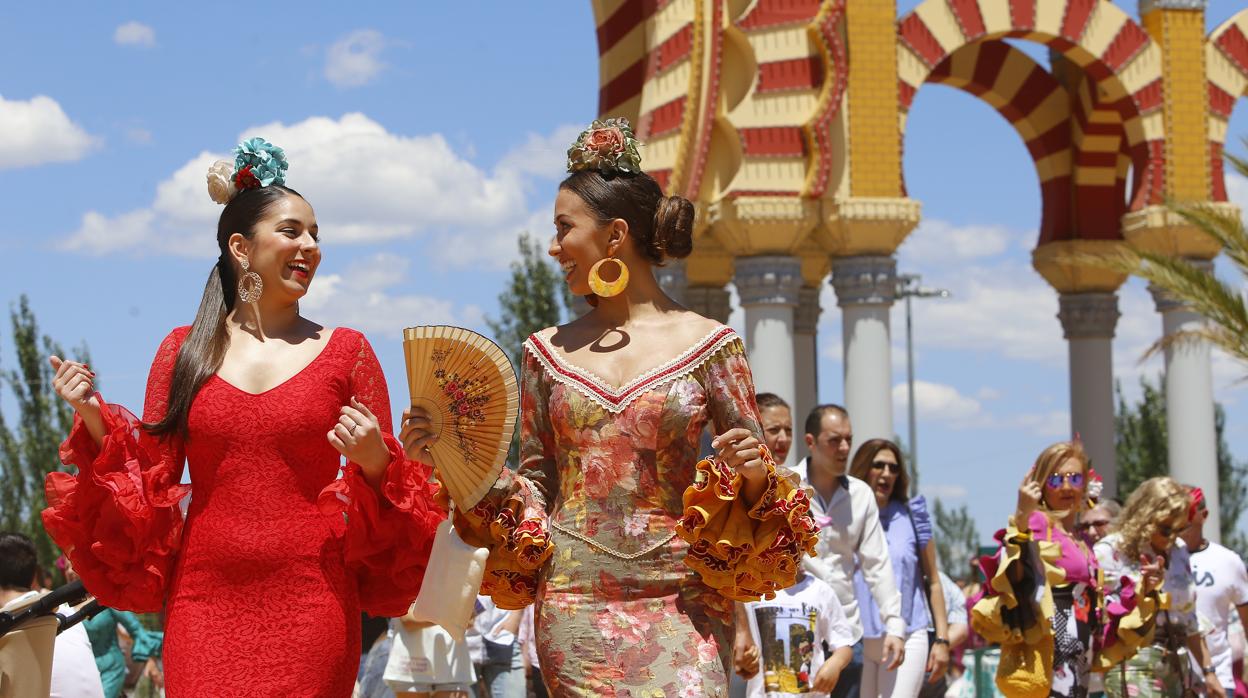 Una mujer se abanica en compañía de una amiga en la portada de la Feria de Córdoba