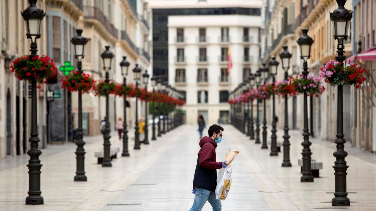 Un joven con mascarilla cruza una calle Larios de Málaga prácticamente desierta