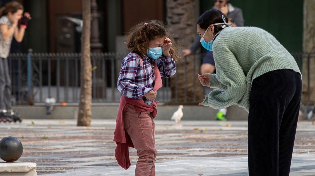 Una niña en patines y con mascarilla conversa con una mujer en la Plaza Nueva de Sevilla