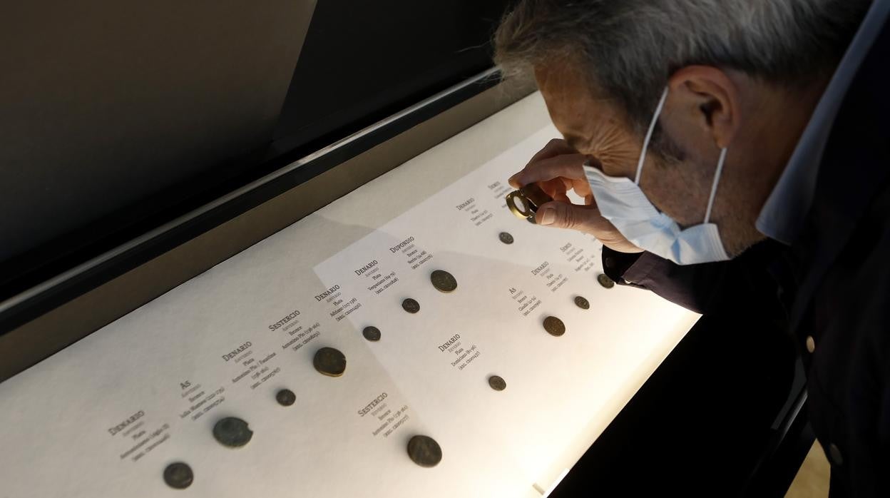 Un hombre examina parte de la colección de monedas que exhibe el Arqueológico