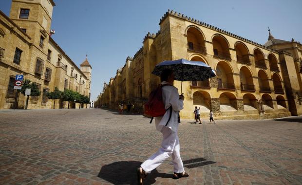 Un turista pasa con paraguas bajo el sol al lado de la Mezquita-Catedral de Córdoba