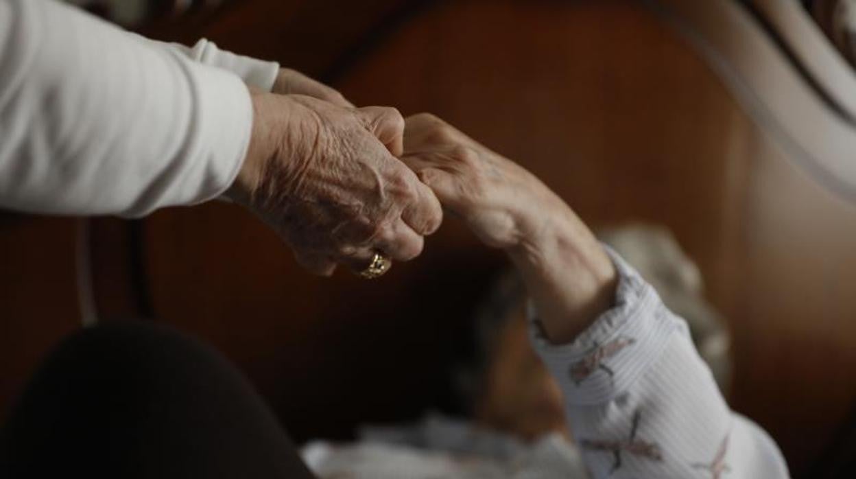 Una cuidadora coge la mano de una anciana dependiente