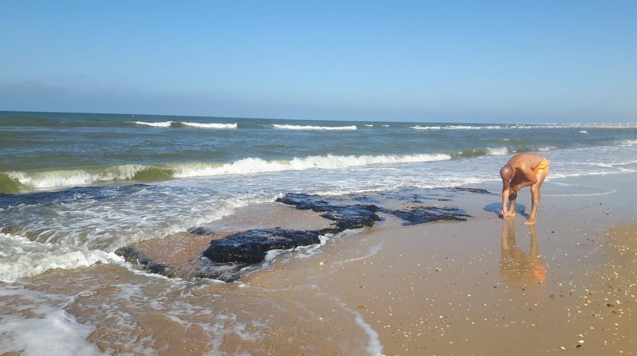 Un bañista toca los restos de la plataforma fósil que deja ver la marea baja en Matalascañas