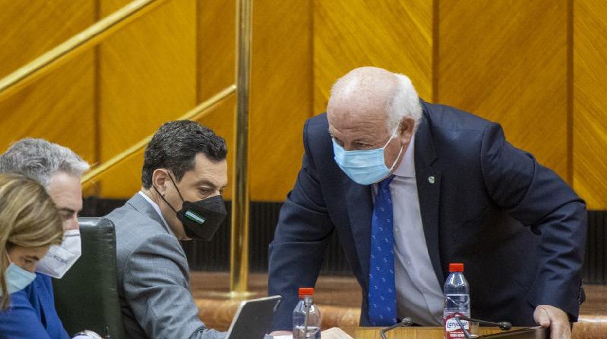 El consejero de Salud, Jesús Aguirre, se acerca a hablar con Juanma Moreno durante el pleno del Parlamento de este jueves