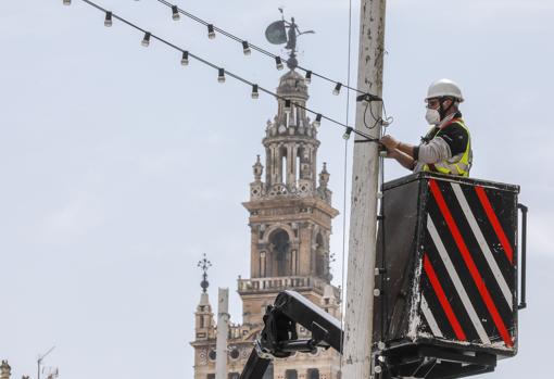 Un operario pone las luces de la Feria en el centro de Sevilla, para aliviar la nostalgia de los sevillanos que se quedan otro año sin disfrutar las fiestas