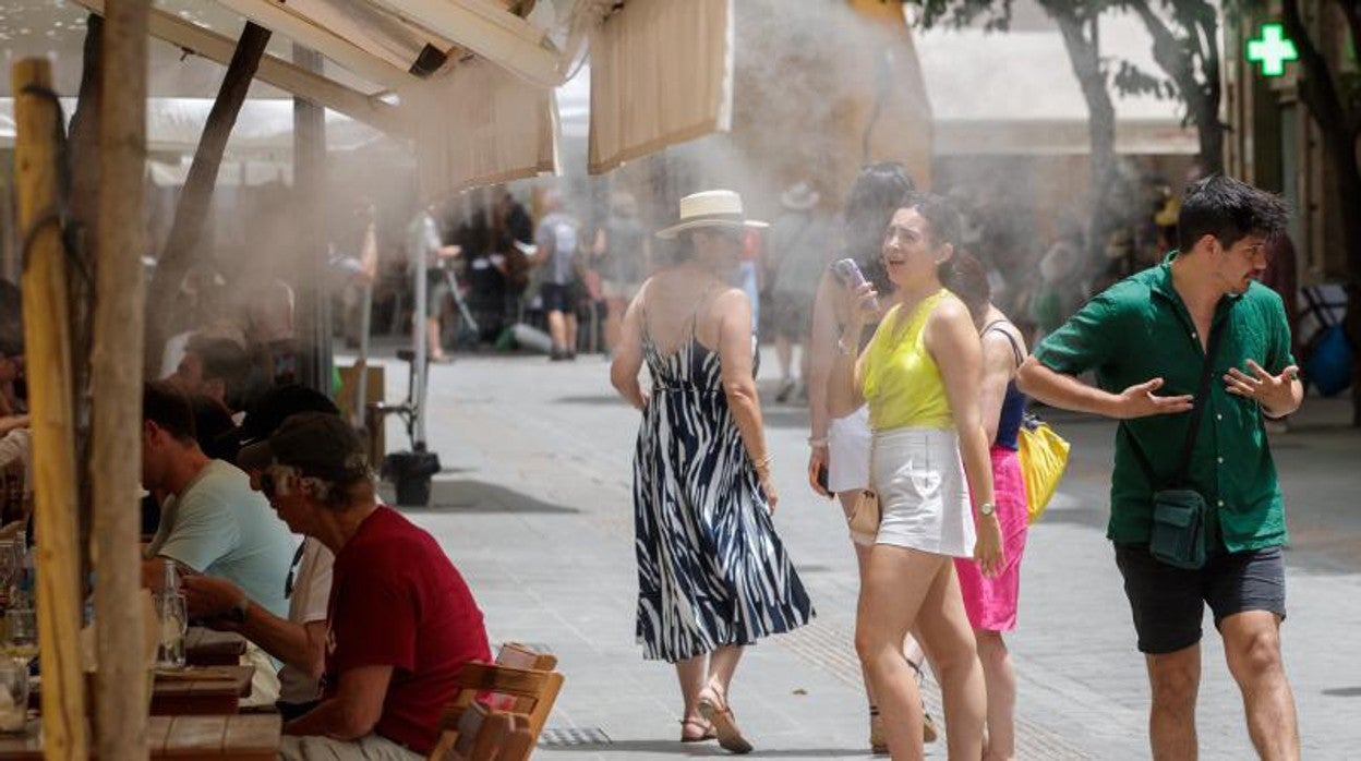 Unos turistas se refrescan con los difusores de vapor de agua de un bar de Sevilla