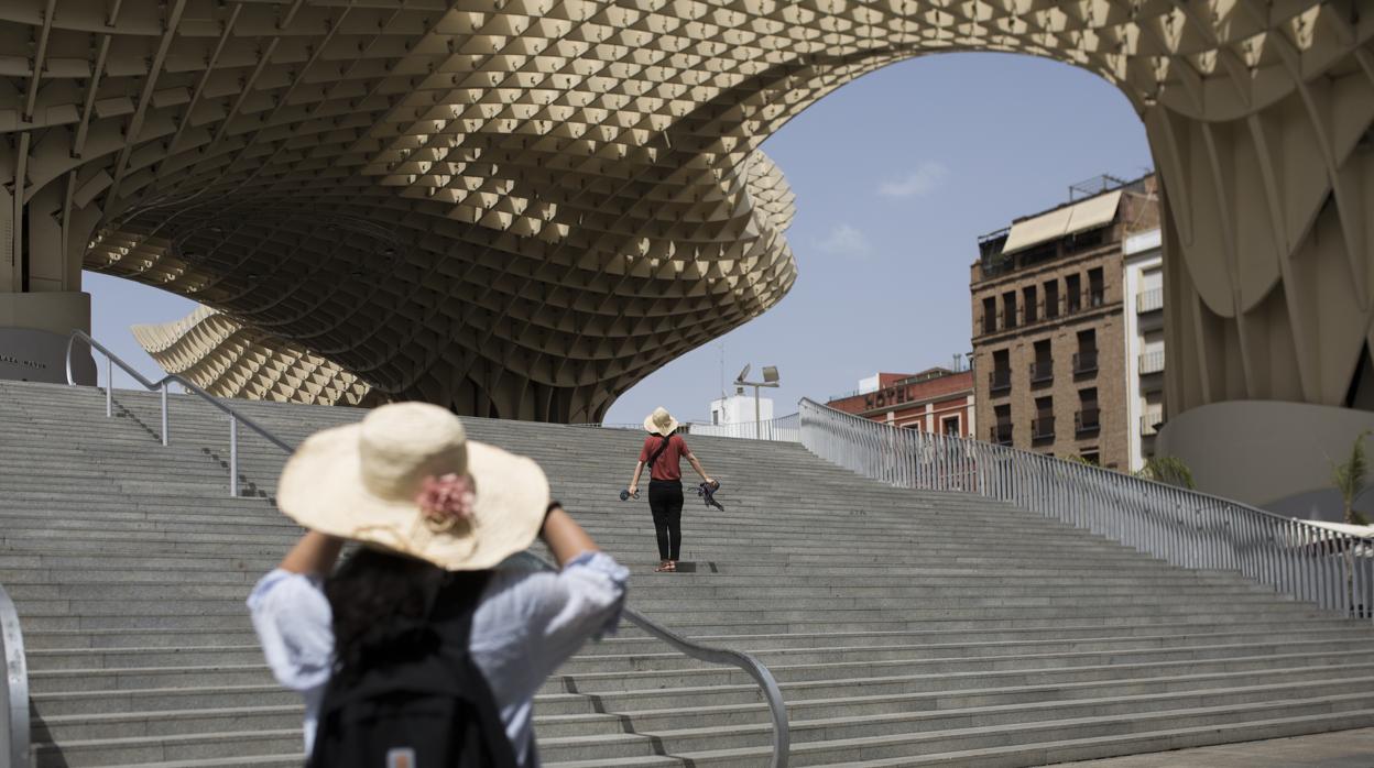Una joven se protege del sol con una sombrilla mientras camina junto a la Torre del Oro