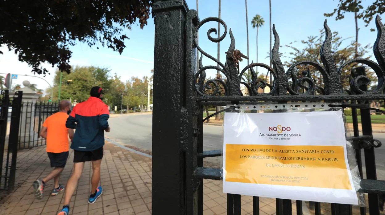 Varios corredores salen del Parque de María Luisa junto a un cartel sanitario