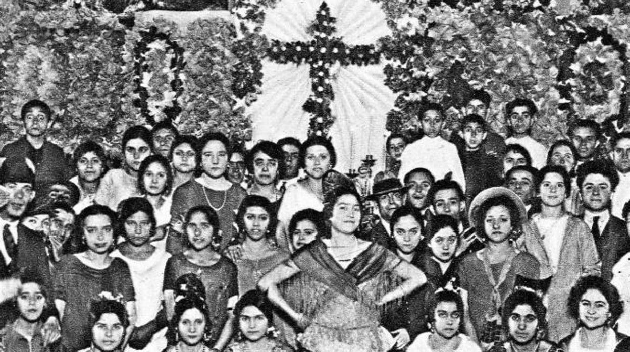 Multitd de sevillanas posando delante de una cruz de mayo