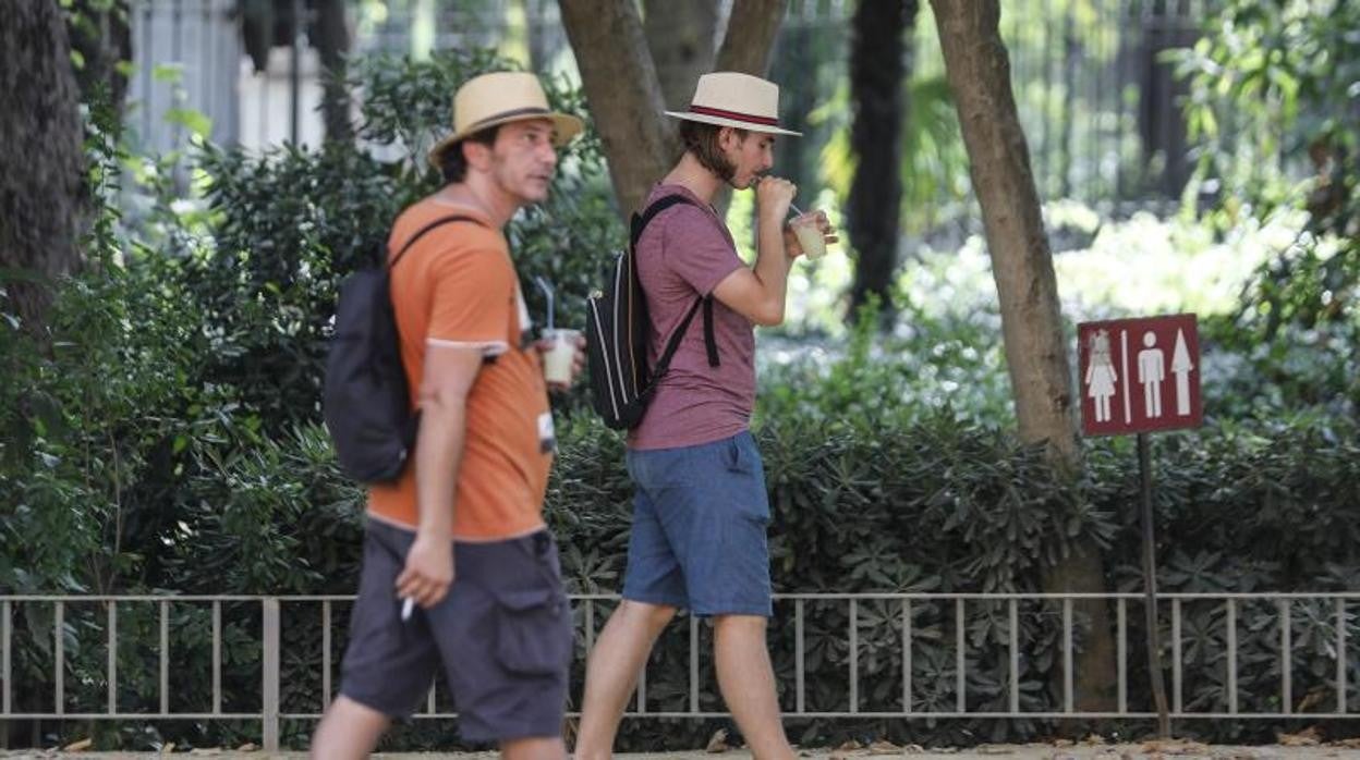 Dos turistas se pasean por el Parque de Masría Luisa