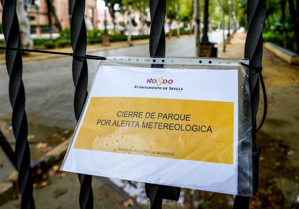 Cartel en una reja de entrada al Parque de María Luisa que indica el cierre por alerta meteorológica