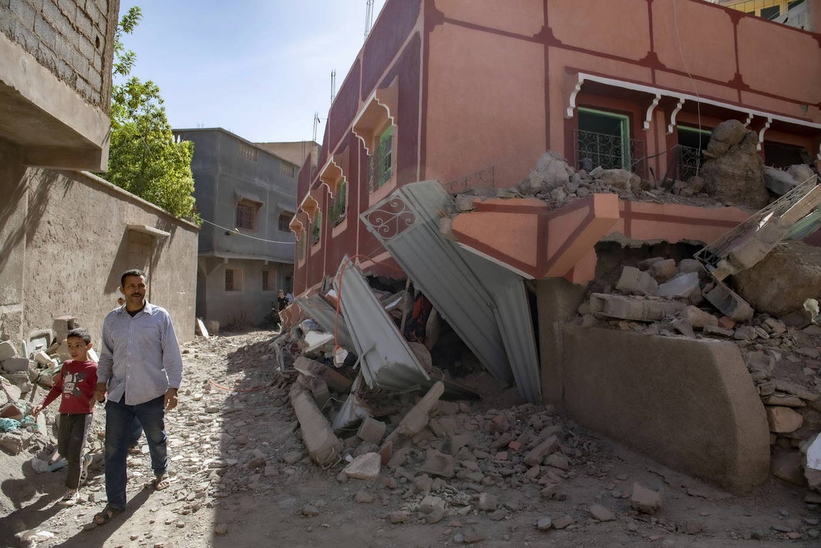 Una persona con un niño camina junto a un edificio dañado tras un terremoto en Marrakech