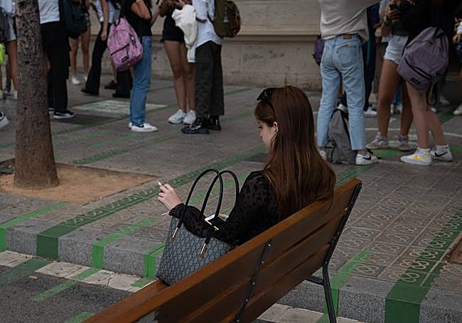 Una mujer fuma sentada en un banco
a la salida del colegio en Barcelona.
