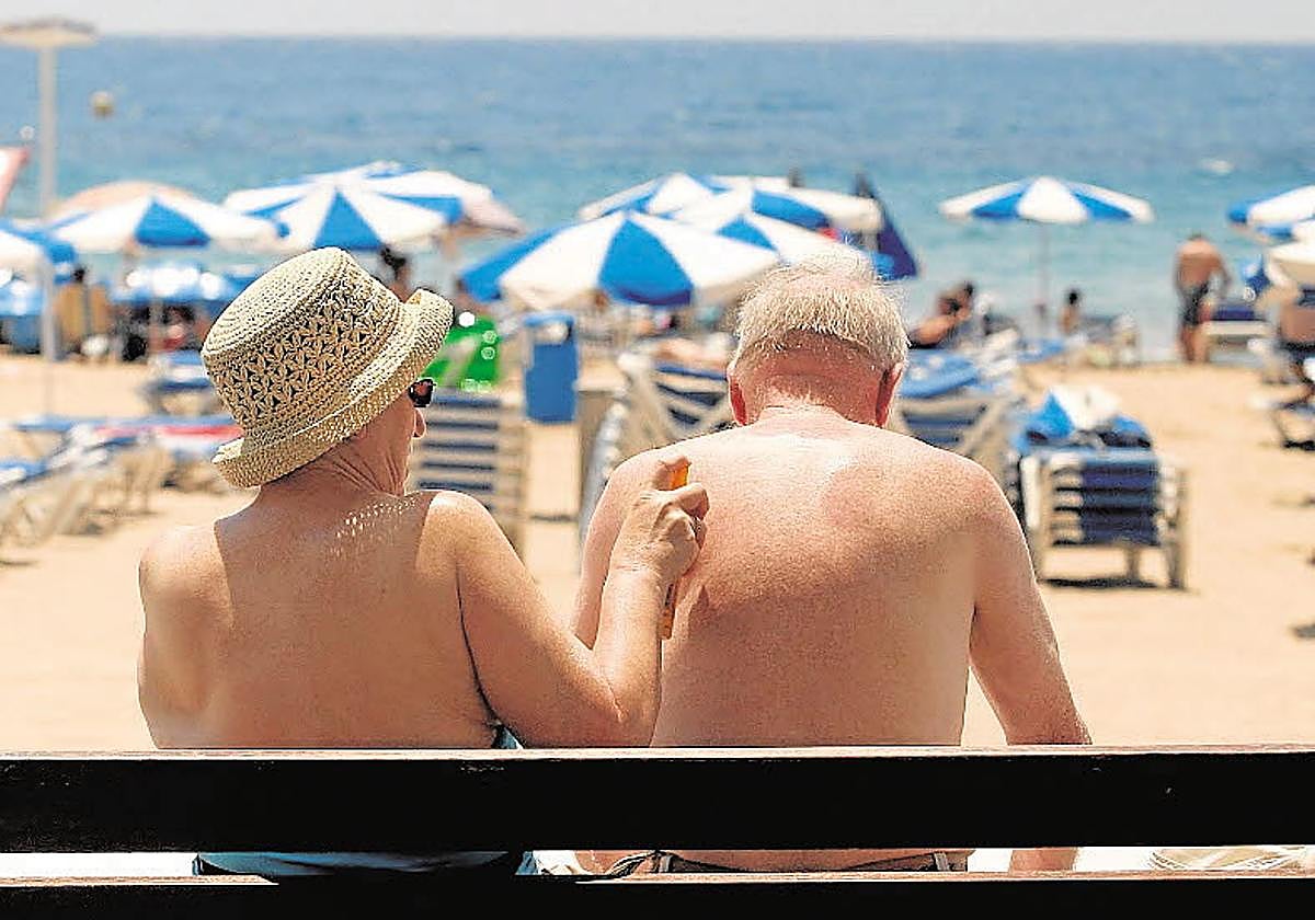 Una pareja de turistas se protege del sol con crema solar en la playa.