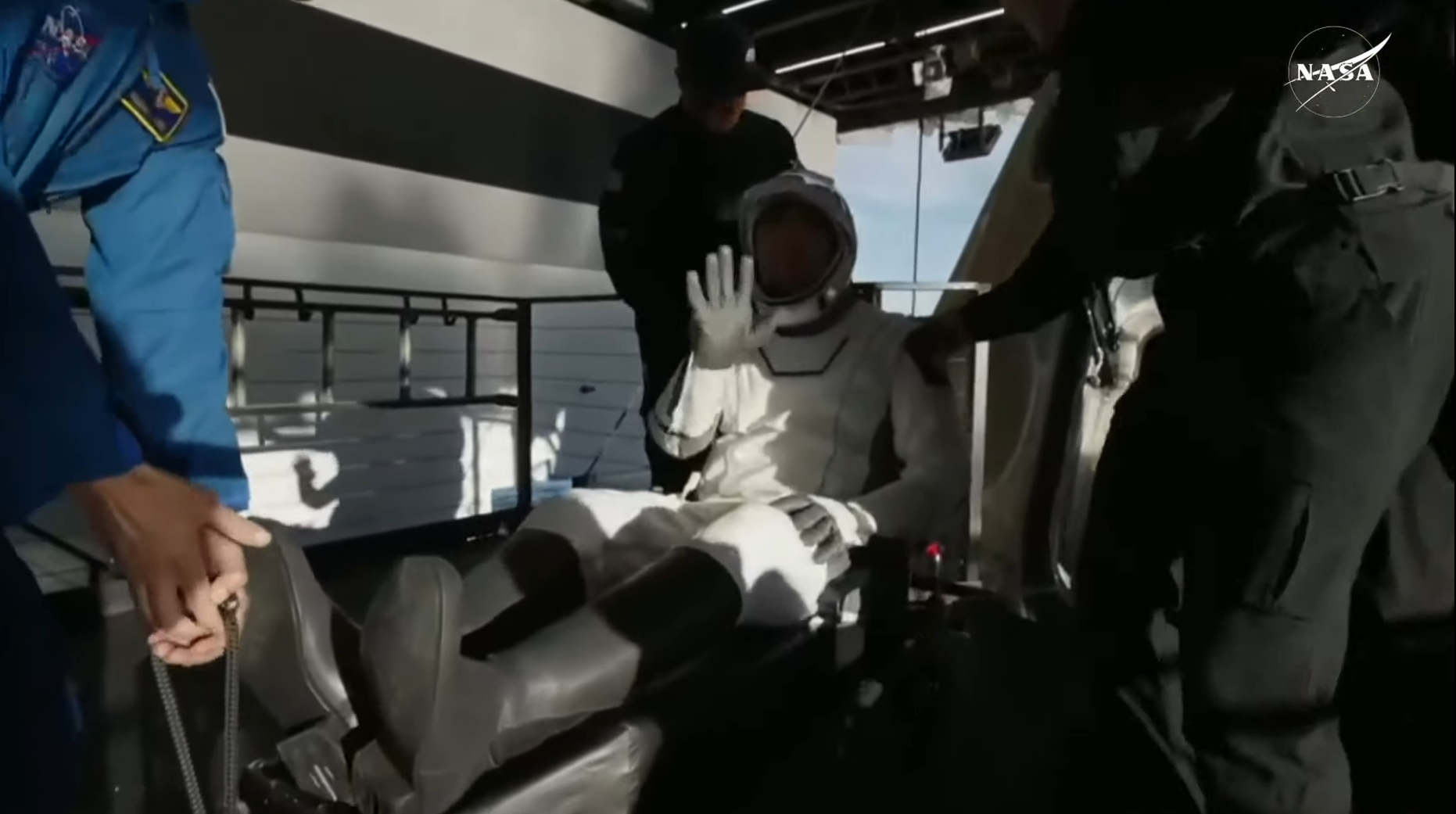 Nick Hague saluda mientras es trasladado sobre una camilla, como es protocolo