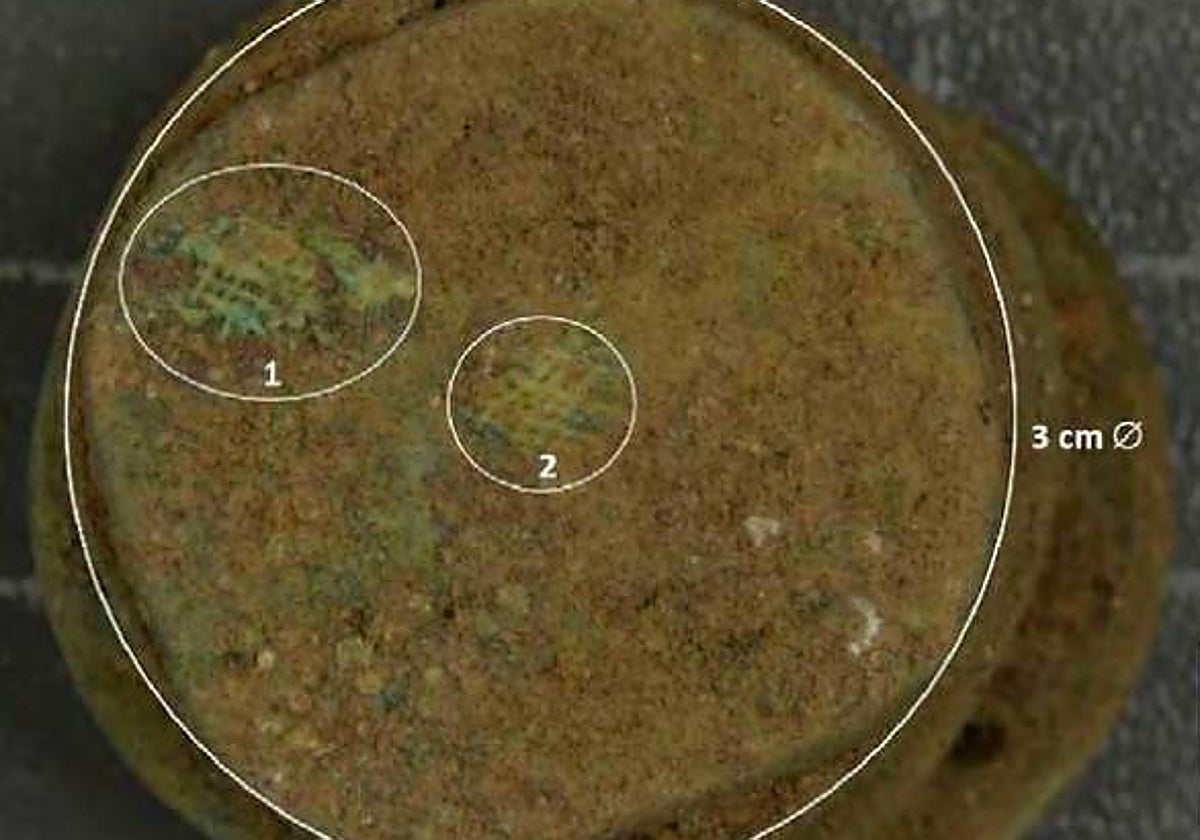 Fragmentos textiles adheridos a una moneda hallada en la Casa del Mitreo