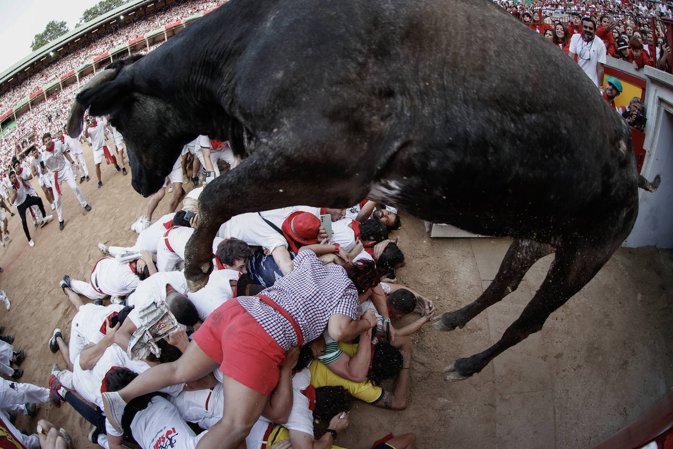 Una vaquilla salta por encima de un grupo de corredores en la plaza de toros tras el tercer encierro de los sanfermines 2023, este domingo en Pamplona