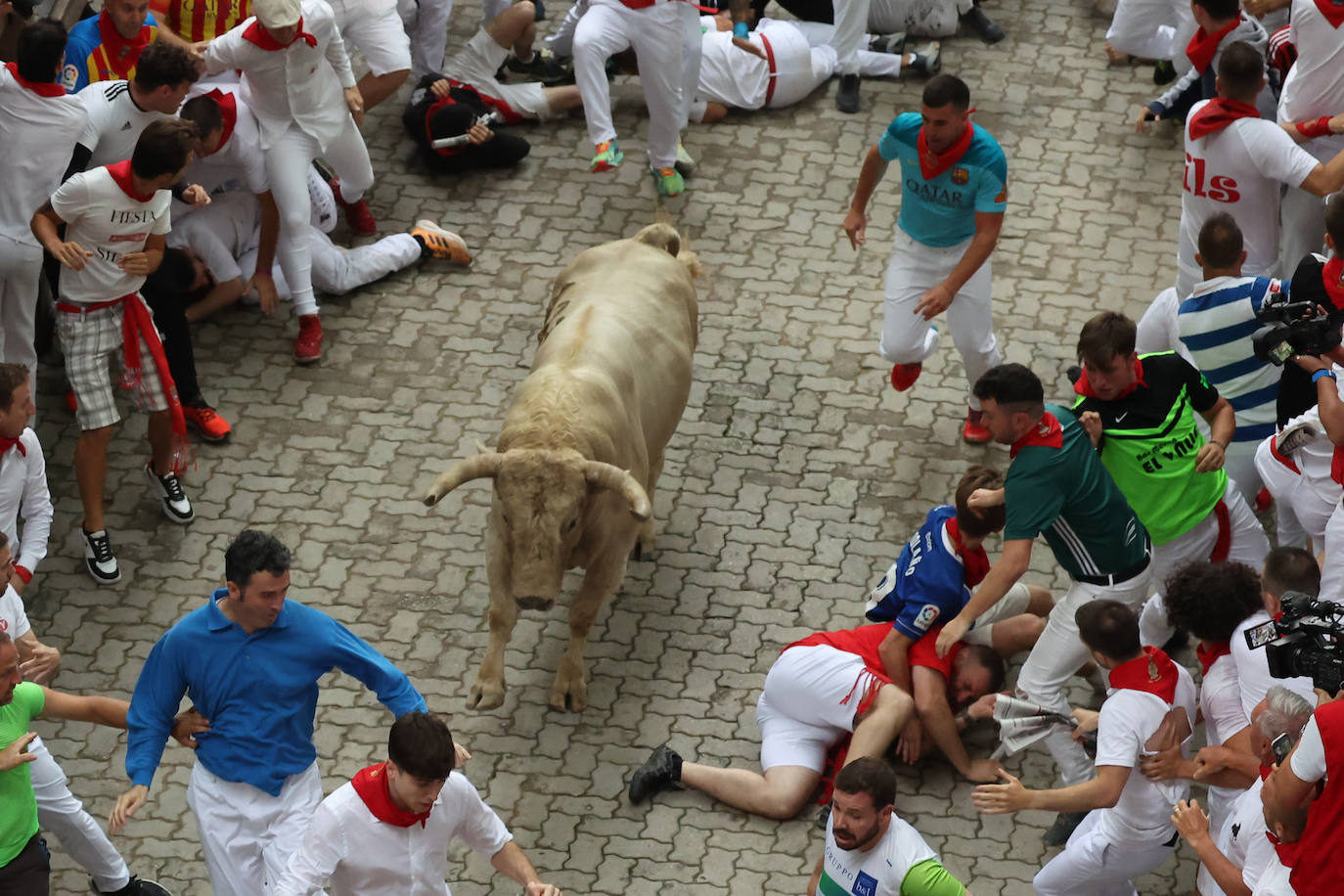 Participantes caen al suelo mientras corren con toros durante el encierro de las fiestas de San Fermín en Pamplona