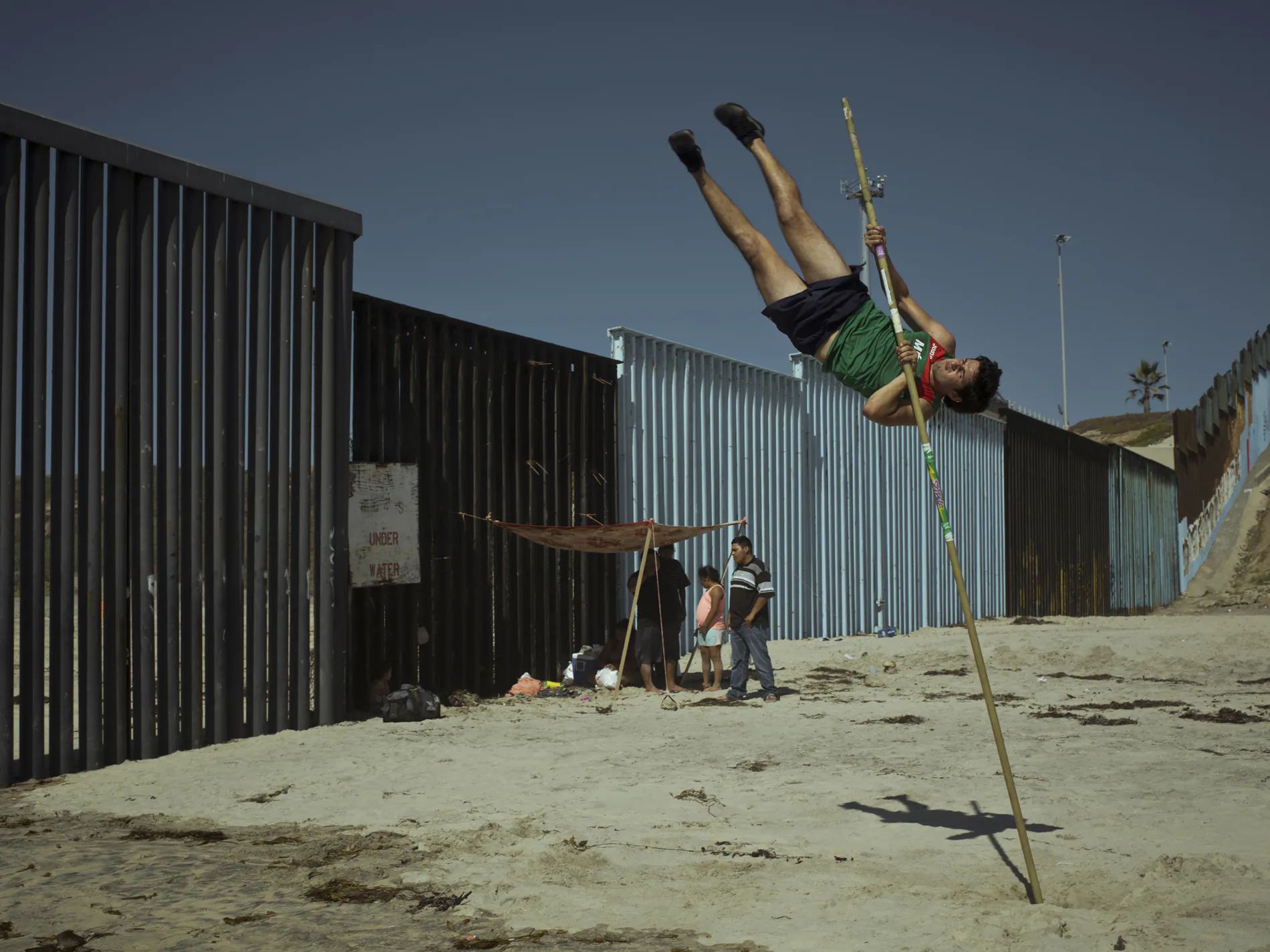 'Atletas de la frontera de San Ysidro'. México. 2018. Jorge Luna, saltador de pértiga profesional mexicano entrena junto a la valla fronteriza en la playa de Tijuana