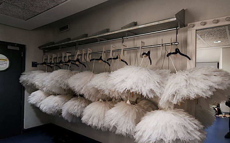 Imagen principal - Mientras que el equipo técnico moviliza todos los tutús de los cisnes con perchas móviles, las bailarinas comprueban el elenco que cada día se imprime y se pone en las bambalinas del Teatro Real
