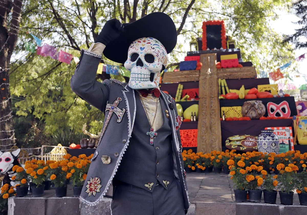 Un hombre disfrazado de catrín frente a una mega ofrenda de Día de Muertos en México