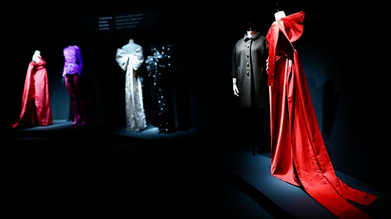 Vista general de la exposición en el museo Balenciaga de Guetaria y en primer plano: top de manga larga de satén de seda rojo atado en la espalda sobre un vestido largo con cola, odelo 42 de la colección de Alta Costura número 51, de Demna para Balenciaga