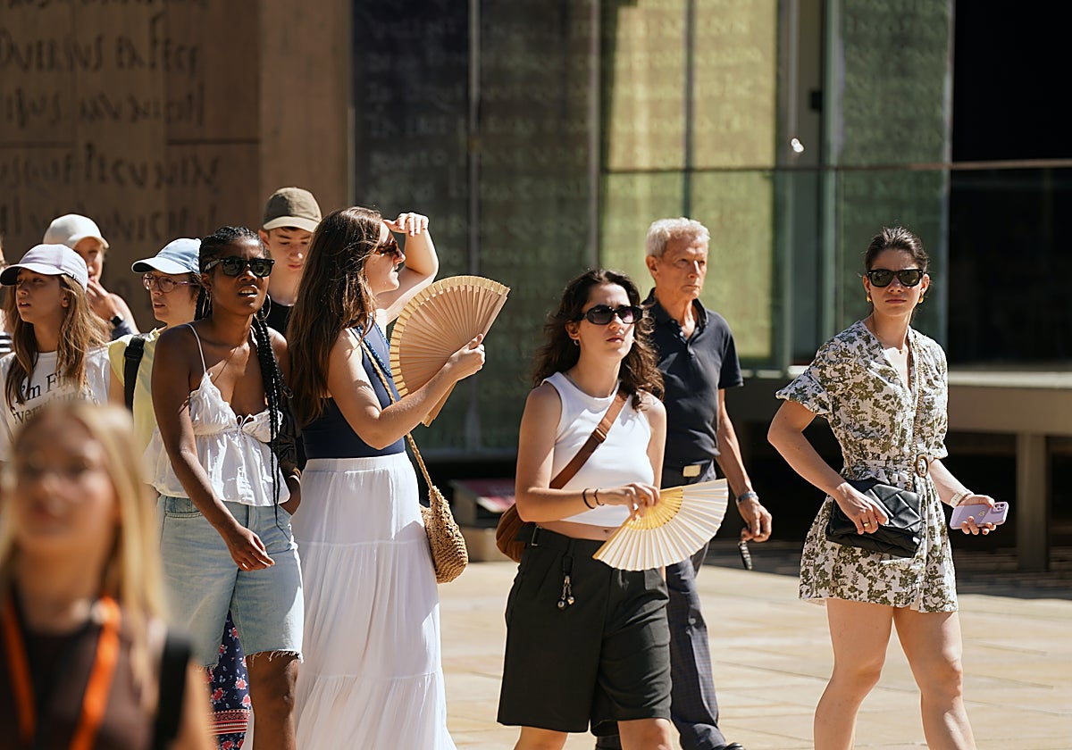 Personas paseando por las calles de Málaga, tratando de combatir el calor con abanicos.