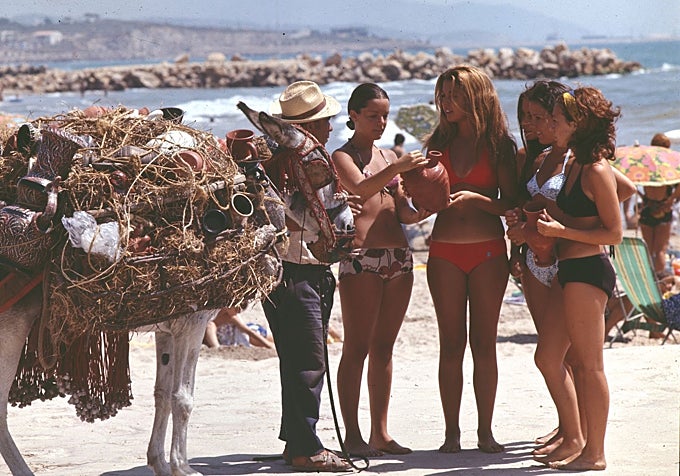 Un vendedor de cerámica con unas jóvenes turistas en bikini, mirando un botijo, en Mallorca en 1966.