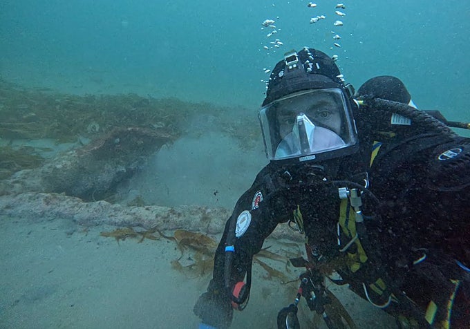 Un arqueólogo subacuático posa junto al ancla