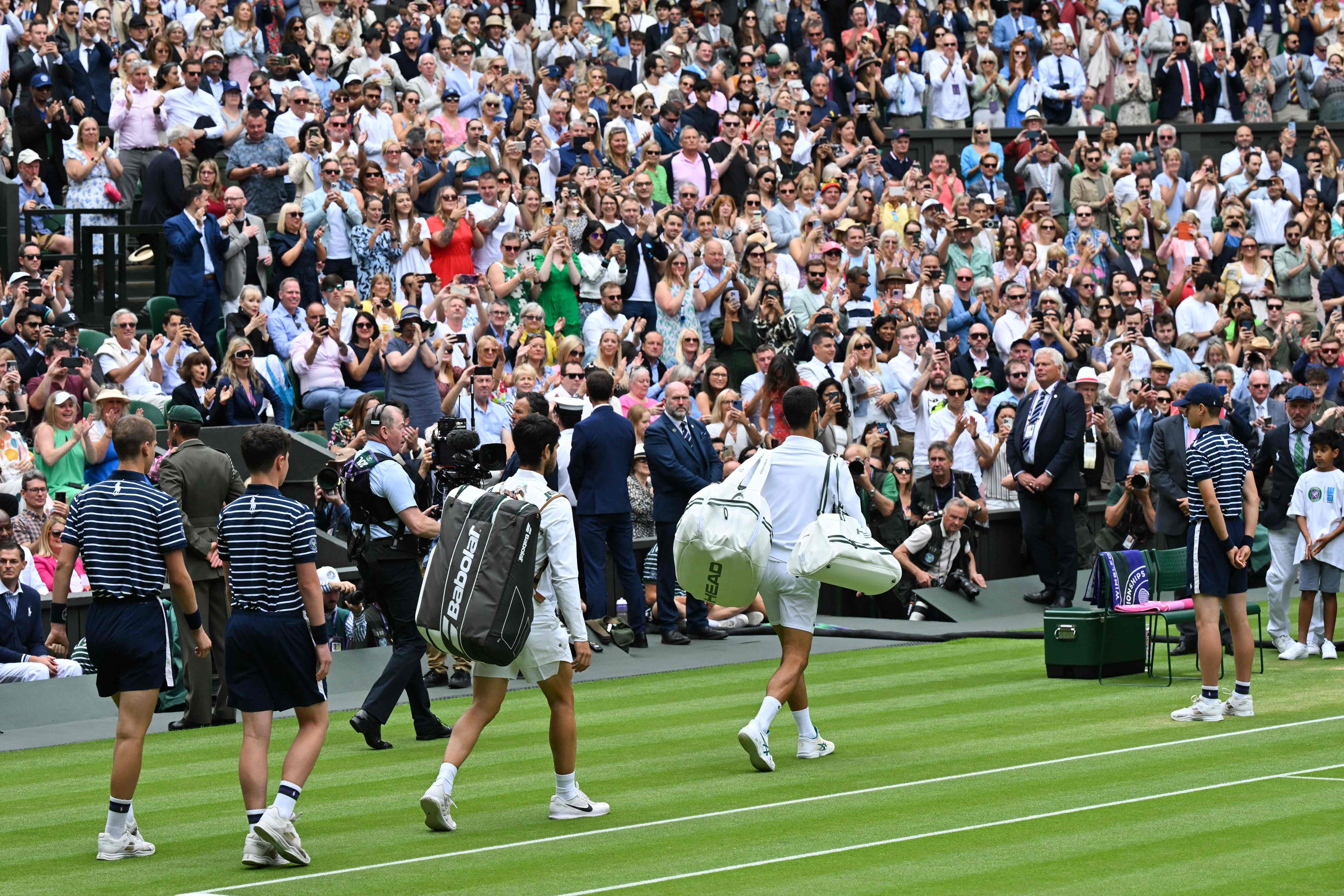 El español Carlos Alcaraz y el serbio Novak Djokovic (derecha) llegan a la cancha para jugar el último partido de tenis individual masculino el último día del Campeonato de Wimbledon 2023 en el All England Tennis Club