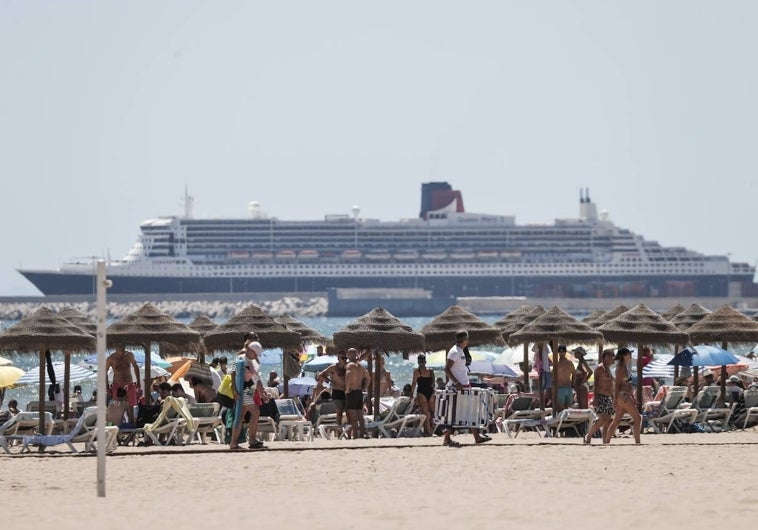 Una playa valenciana llena de turistas, con un crucero de fondo