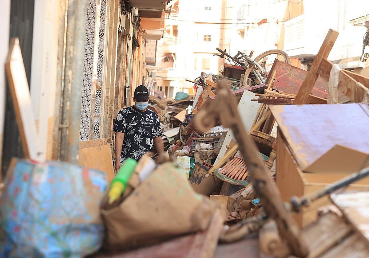 Un hombre pasa frente a muebles y escombros tras el paso de la DANA en Catarroja